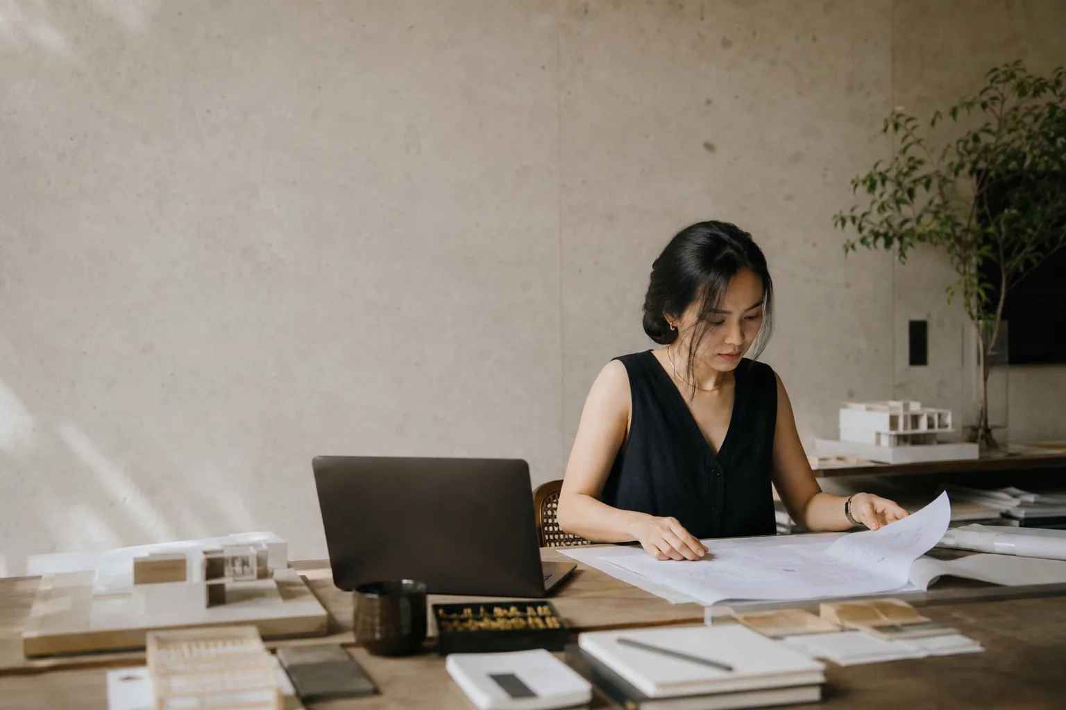 Một kiến trúc sư đang làm việc với bản vẽ và mô hình trong studio